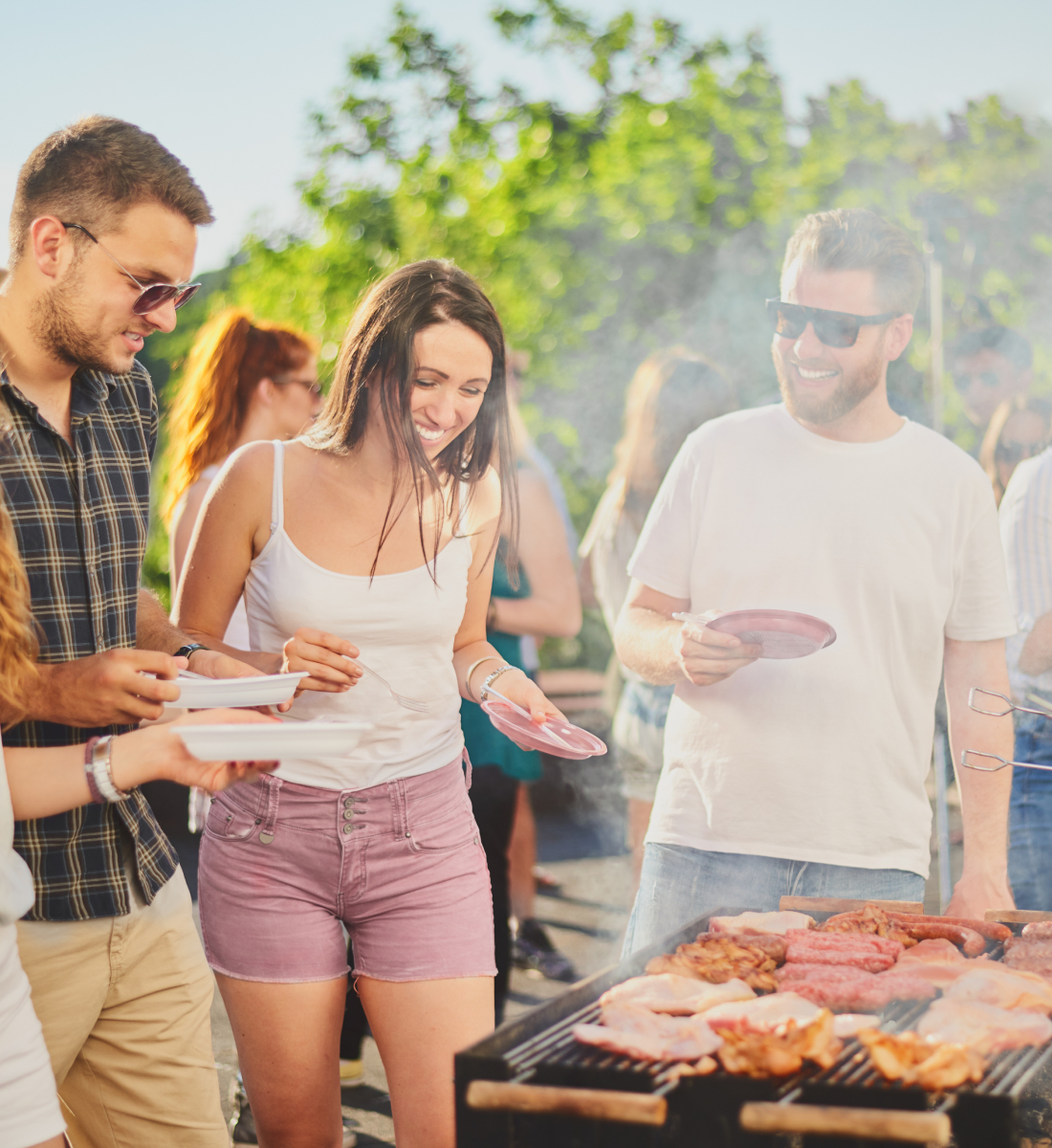 adults standing around grill while food cooks