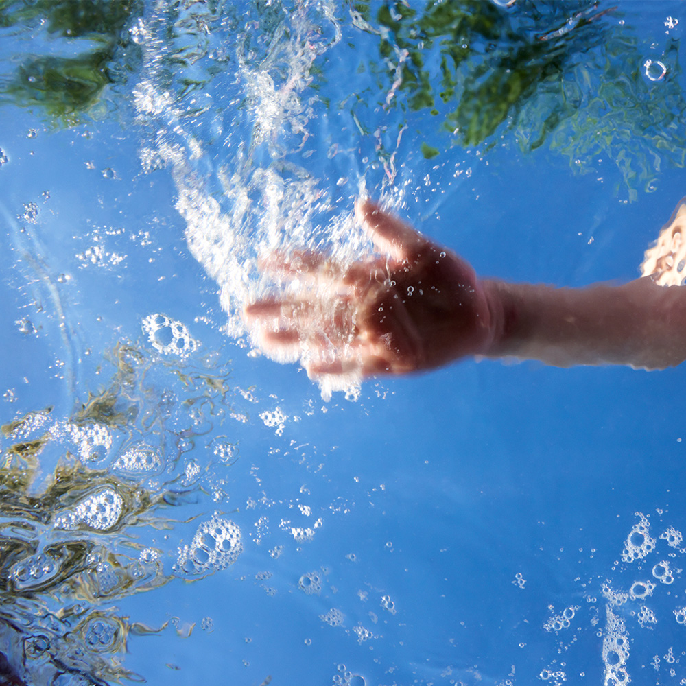 Hand skimming crystal clear water with blue sky in background.